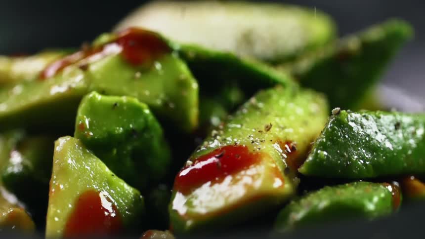 A piled of cut avocado with sauce on top of it has seasoning sprinkled over the top of it