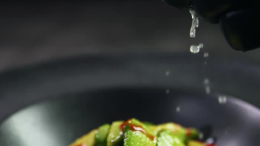 The cook squeezes a lime into the sliced avocado topped with chili sauce