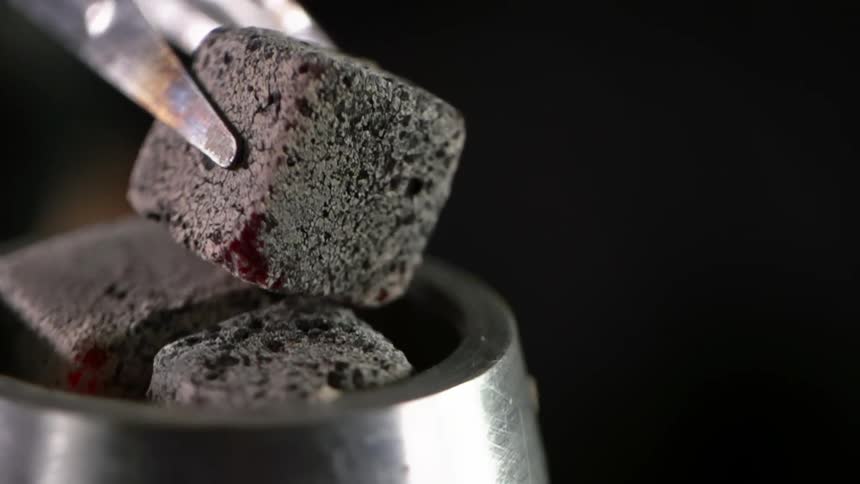 A person places a heated charcoal cube in a metal bowl