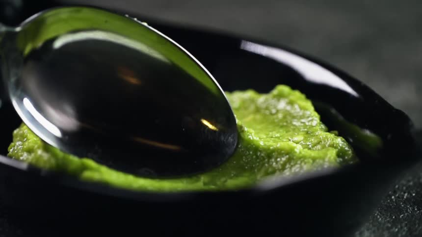 A spoon is used to smear a guacamole on a black plate