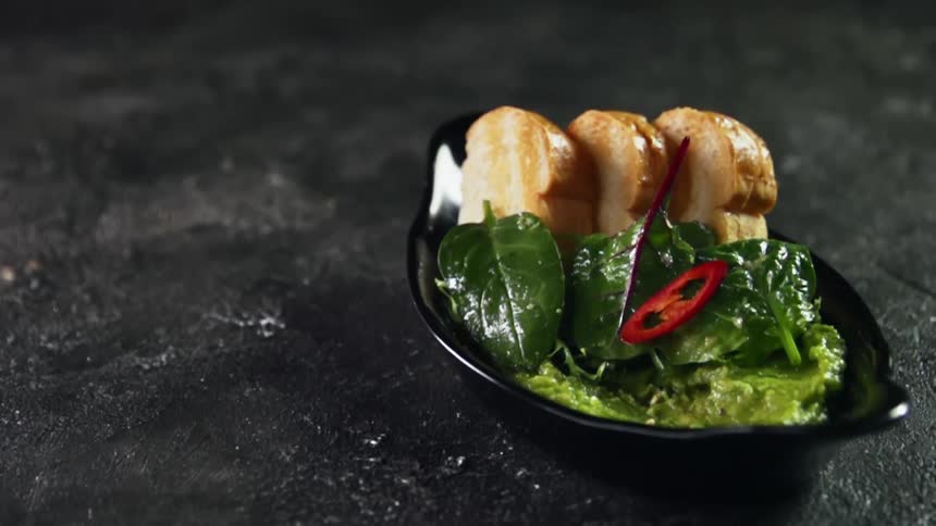 Sliced red chili peppers are dropped onto green salad in plate with toasted bread and guacamole