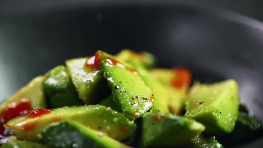 Seasoning falls onto avocado chunks in dish