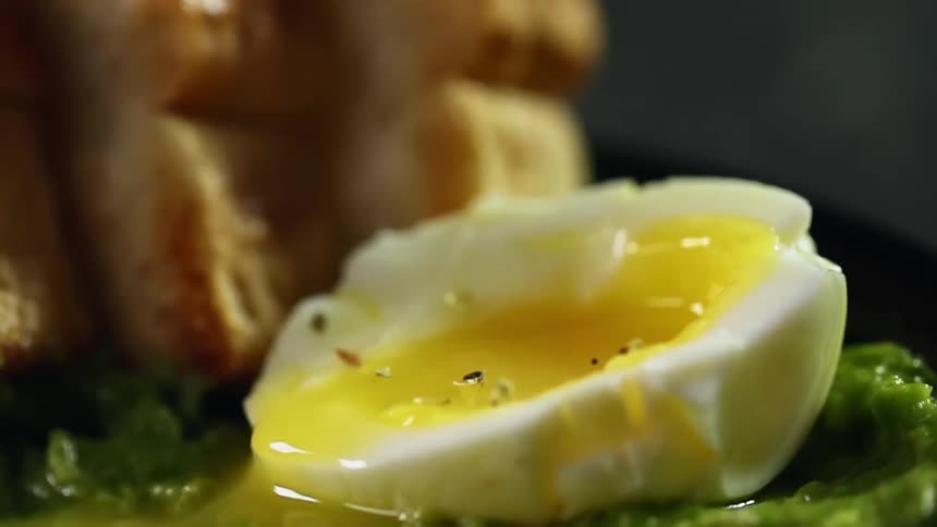 A soft boiled egg cut in half with runny yolk over lettuce being seasoned