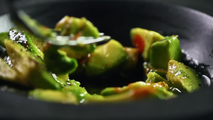 Avocado and sauce in a black bowl being mashed with a fork