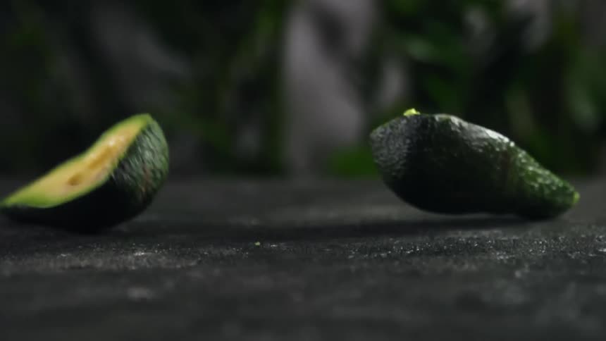 Sliced avocado drops onto hard grey surface and splits in half