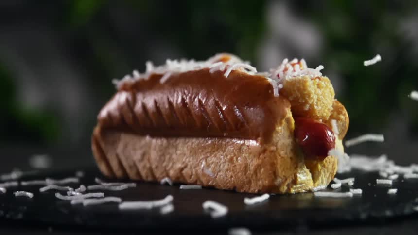 Shredded onion falling on and around a hot dog