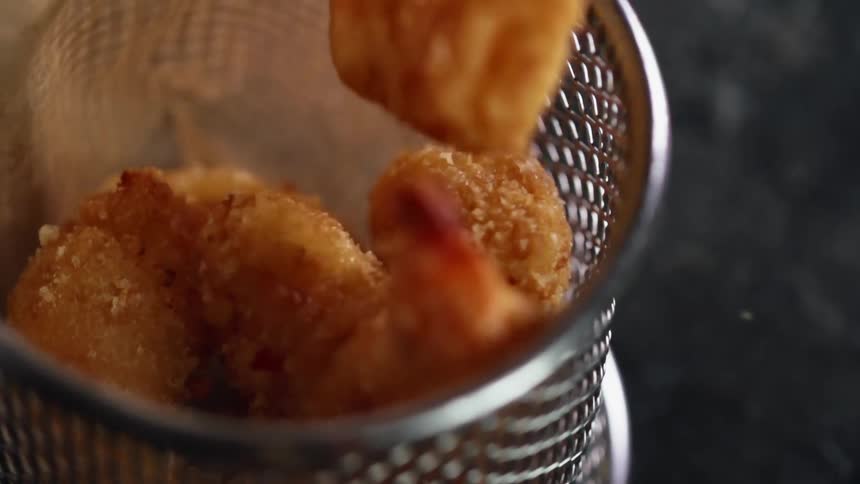 Fried shrimps coated in breadcrumbs are dropped into a metal basket lined with thin paper