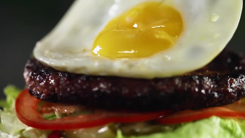 Fried egg gently place on top of a grilled burger patty sitting on a bed of  lettuce and thinly sliced tomatoes