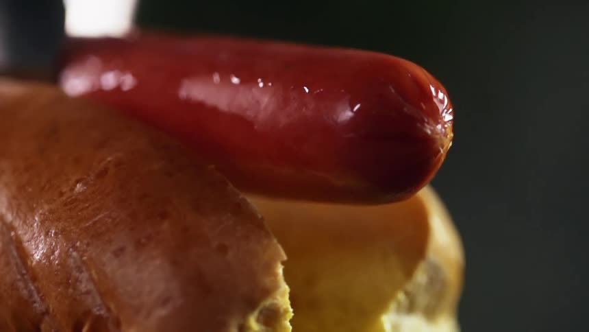 Metal tongs place sausage into the opened brioche hot dog bun
