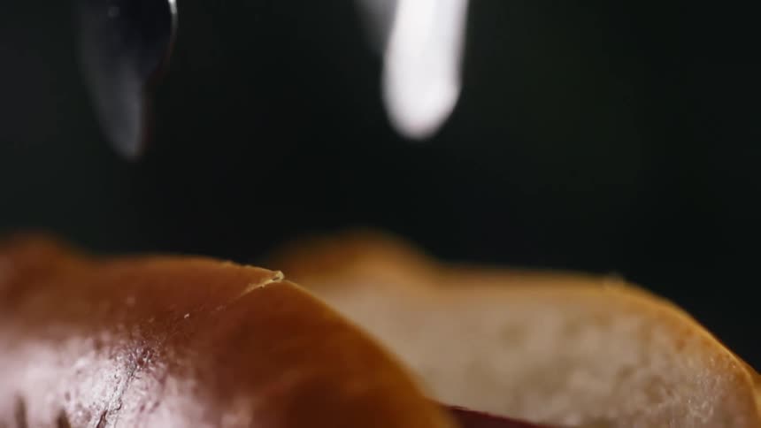 Sausage is being dropped into a hot dog bun