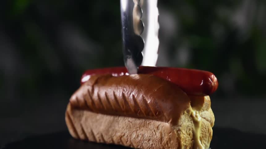 Placing a sausage inside a hot dog bun with a tong