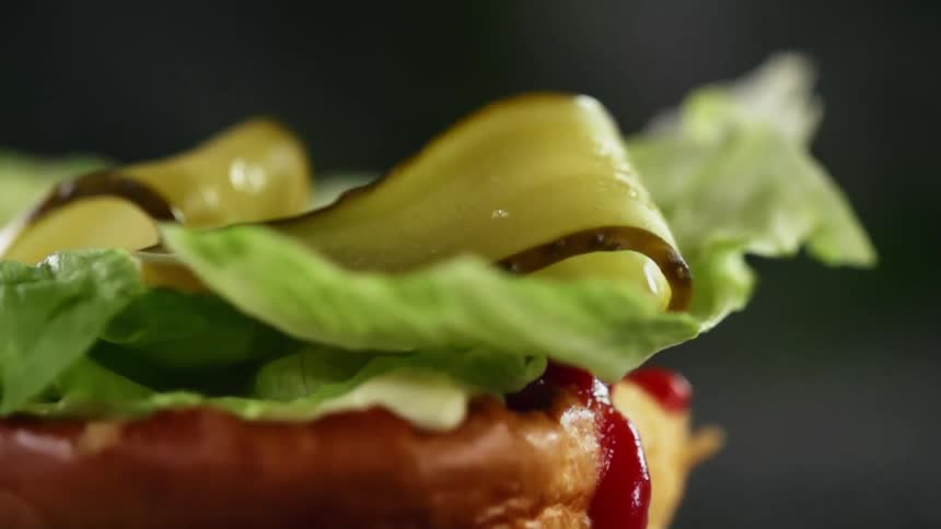 Pickles falling onto a bread bun with ketchup and lettuce