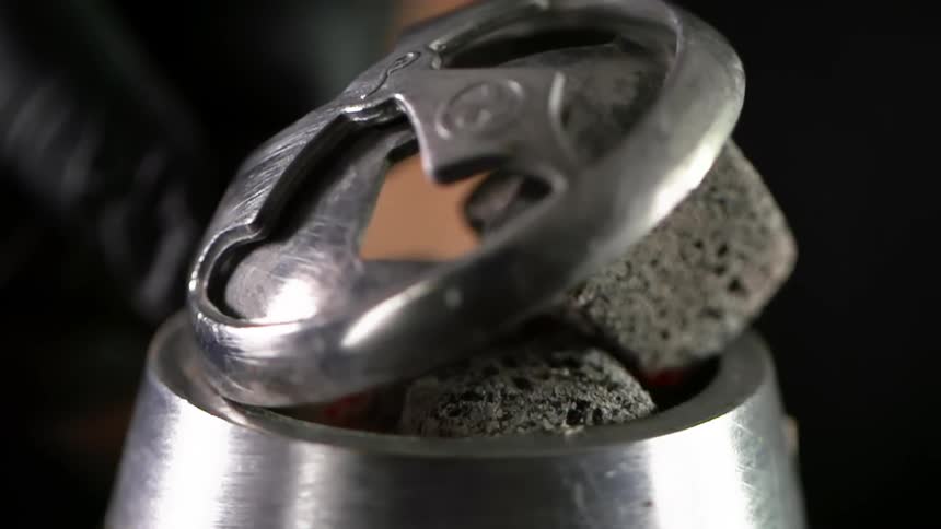A person puts a lid on a metal bowl with heated charcoals in it