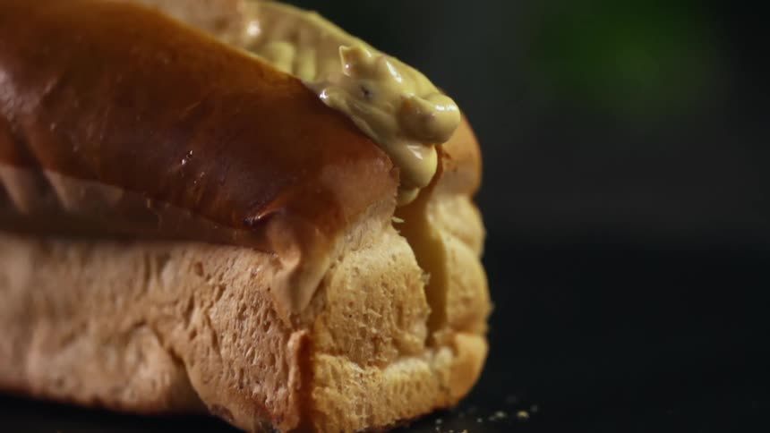 Mustard being put in a hot dog bun