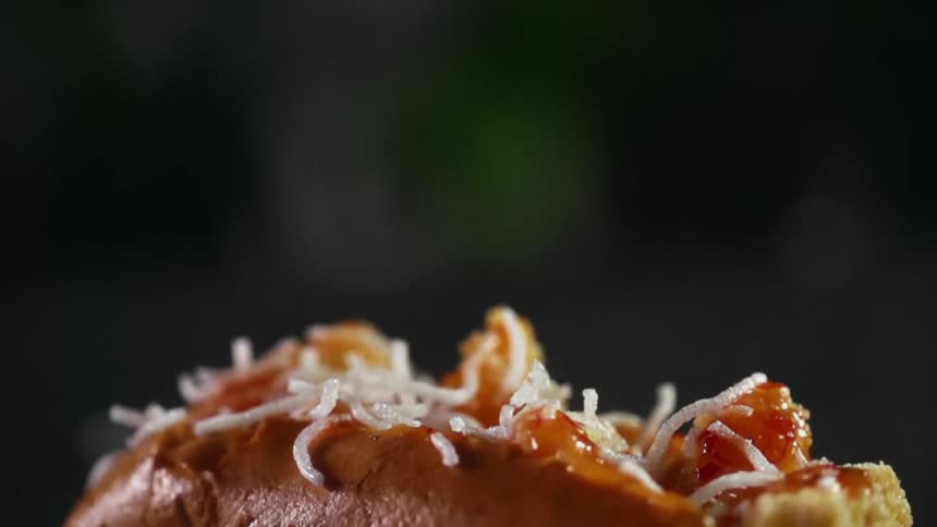 Shredded cheese is sprinkled over the top of a hot dog
