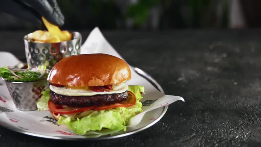 Hand picks up french fries from a metal container next to a hamburger