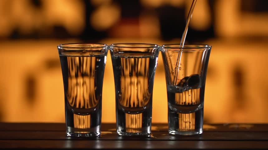 Clear liquor being poured on small glass shots over a counter