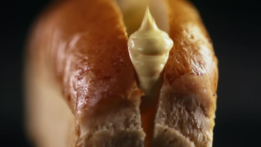 Mustard is dripped into a brioche hot dog bun
