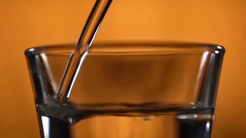 Liquid is being poured into a glass with an orange background