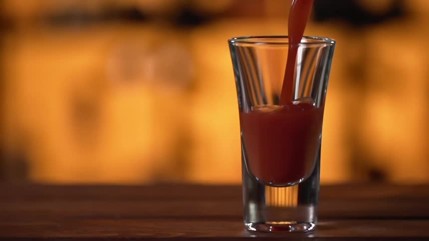 A red liquid is being poured into a glass in a bar