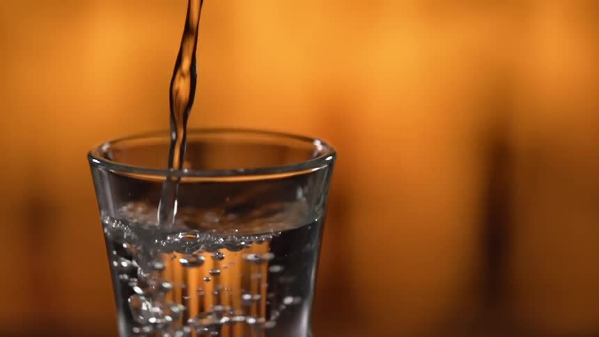 Clear liquor being poured in a clear glass shot against a yellow background