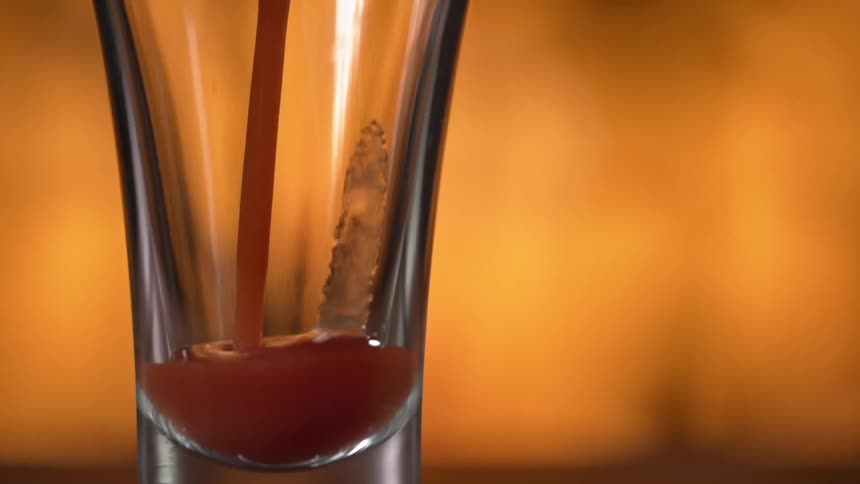 Red juice is being poured into a glass in a bar