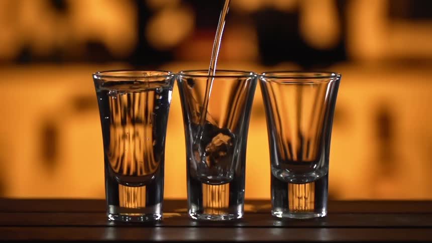 Liquor is poured into three shot glasses on a bar counter