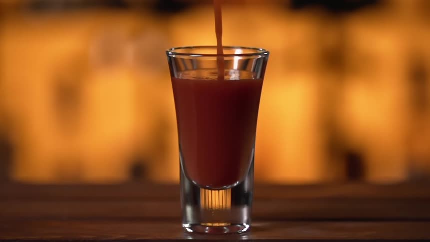 Red juice is being poured into a glass in a bar