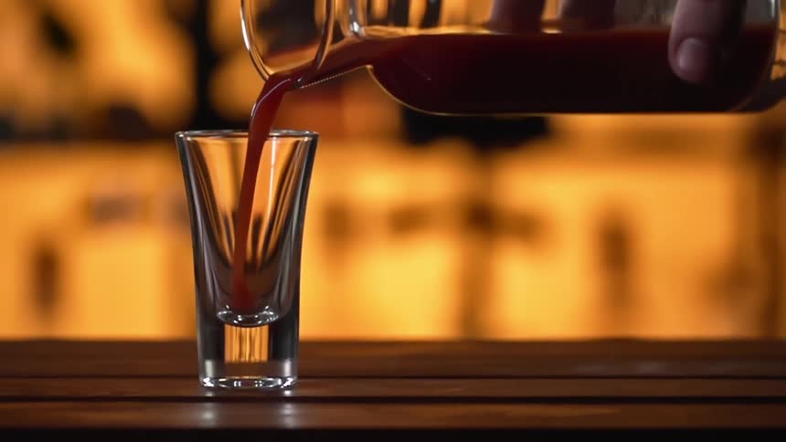 A person pours a drink in to a shot glass