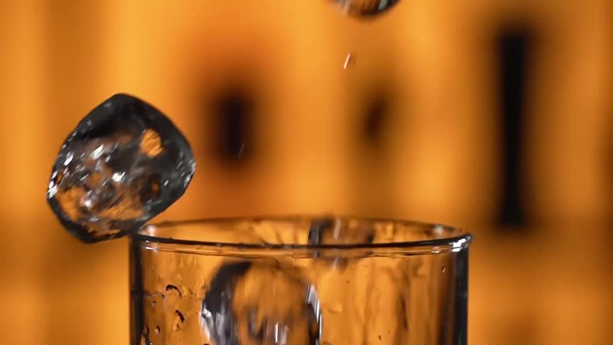 Ice cubes being dropped into a glass in a bar