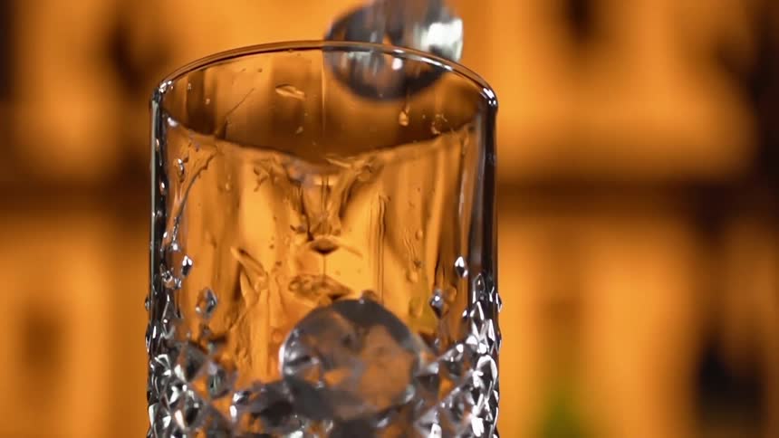 Ice cubes are dropped into a glass in a bar