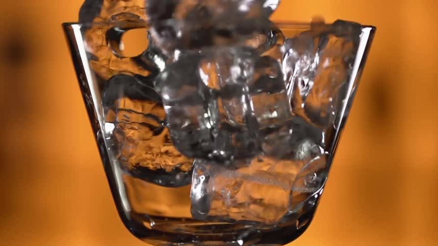 Ice cubes are being dropped into a glass in a bar