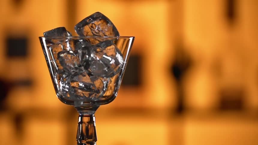 Ice cubes are dropped into a glass in a bar