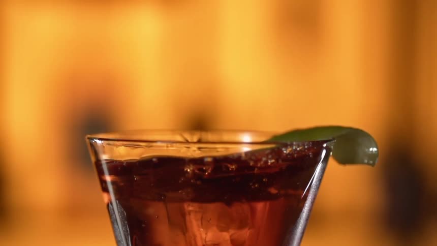 An ice cube is dropped into a cocktail glass causing liquid to splash up