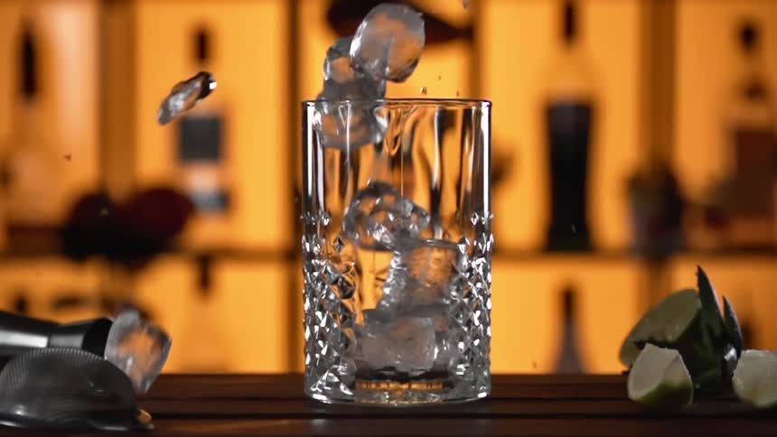 Ice cubes drop into a clear glass from above