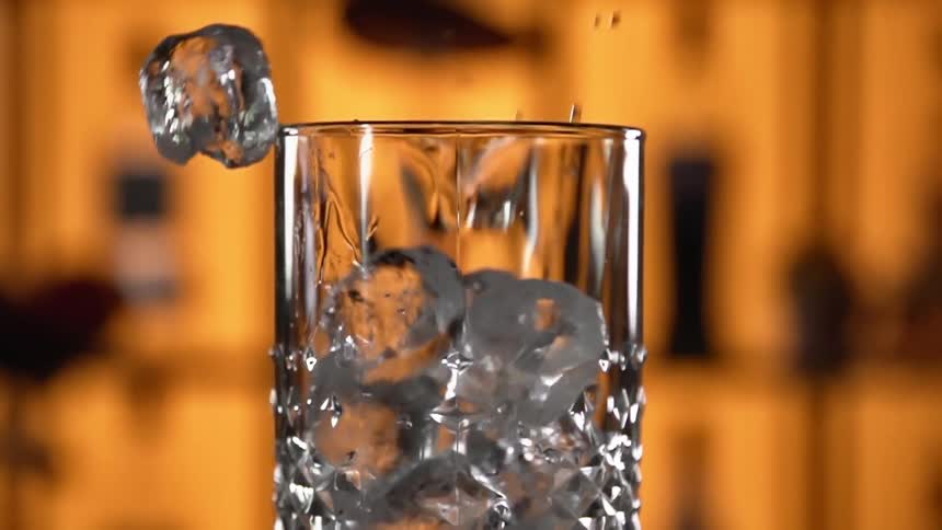 Ice cubes are being dropped into a glass in a bar