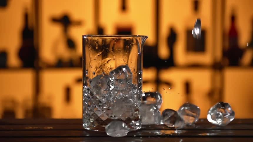 Ice cubes are being dropped into a glass on a counter in a bar