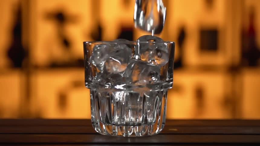 Ice cubes falling into a drinking glass on a wooden counter