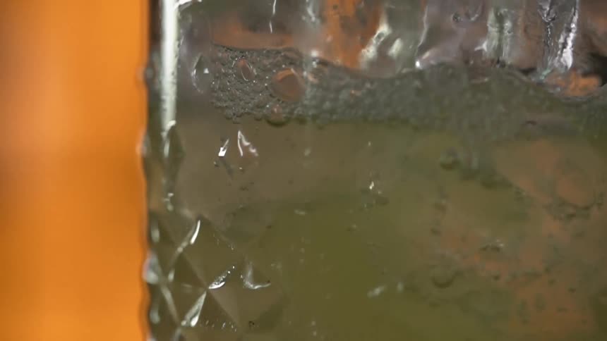 Carbonation bubbles rise in a glass as a cocktail is poured over ice