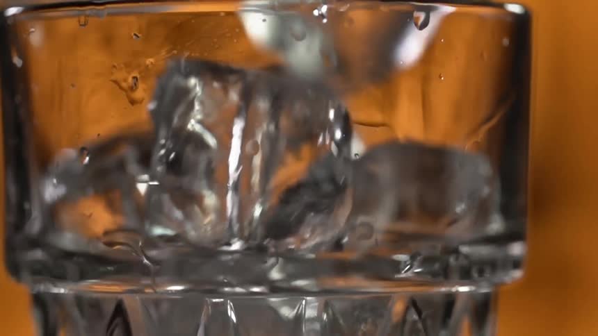 Ice cubes fall into a glass over a counter