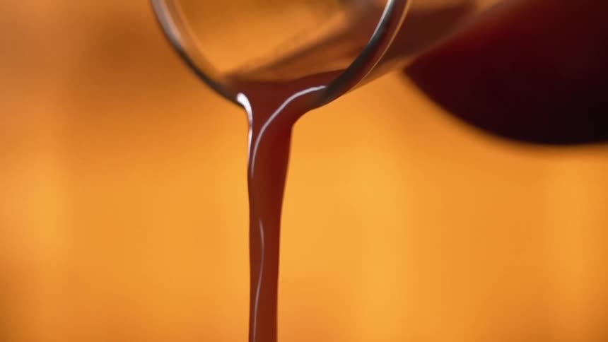 Red wine is poured out of a glass carafe