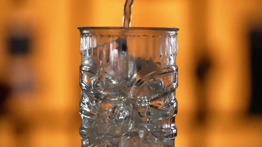Close up of a liquid being poured into a glass with ice cubes in a bar
