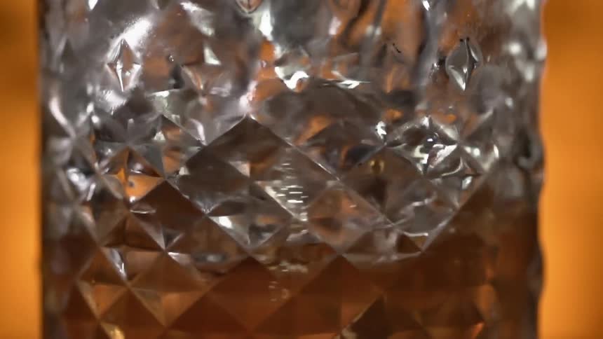 A glass with brown liquid and ice being stirred with a spoon