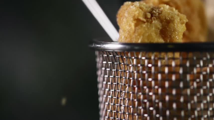 Nuggets that are covered in breadcrumbs are dropped into a metal basket