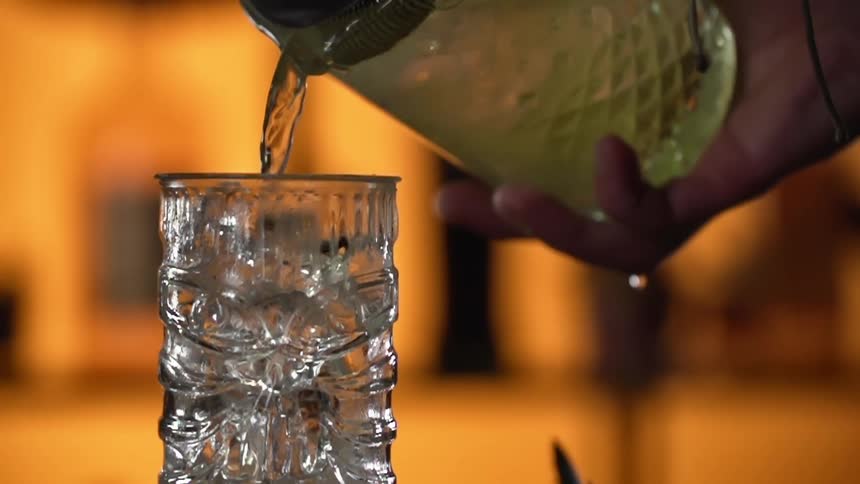Person pours liquor from a bottle into a glass in a bar