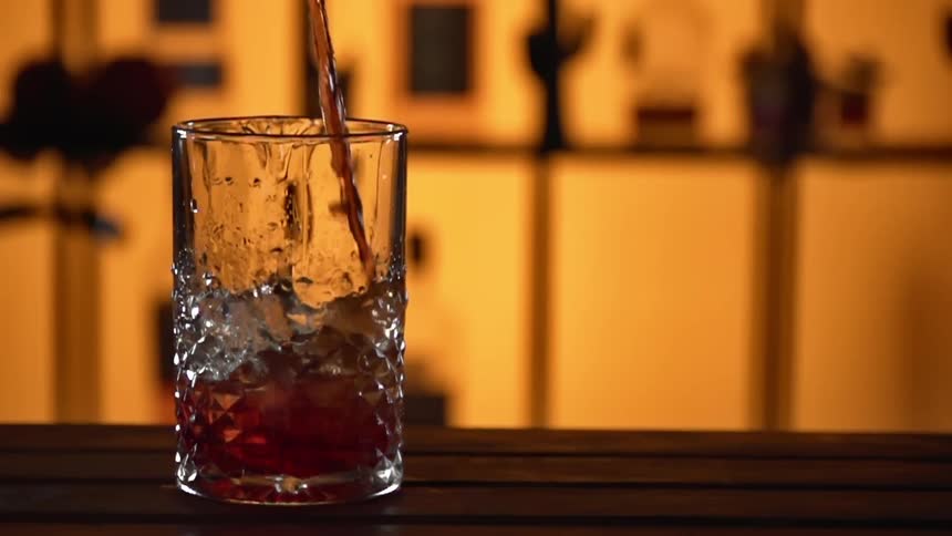 A red liquid is being poured into a glass with ice cubes in a bar