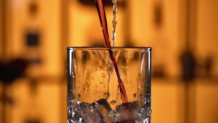 Two ingredients of a cocktail pour from jiggers into a drinking glass filled with ice
