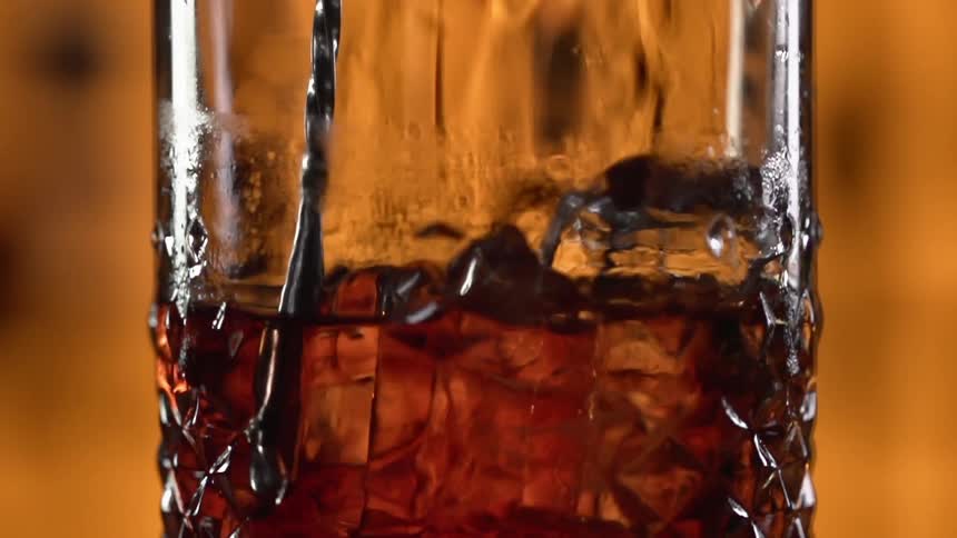 A drink with ice cubes is being stirred