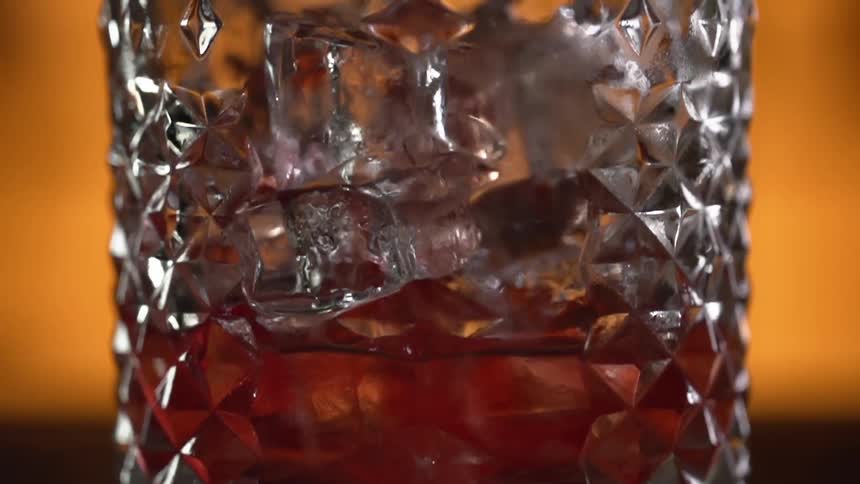 A drinking glass being filled with a reddish liquor