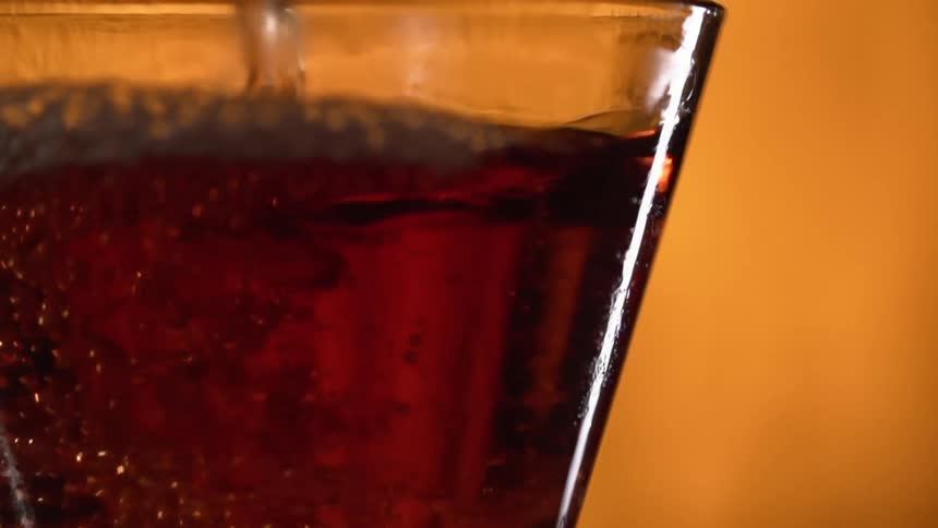 A brown liquid is being poured into a glass with an orange background